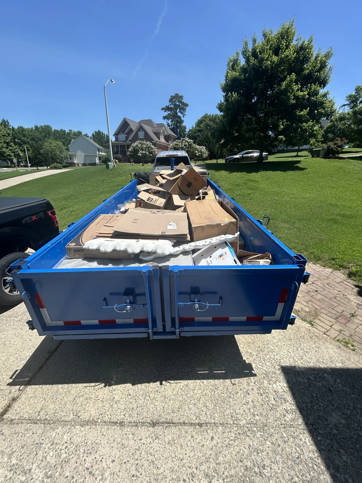 Loaded blue ACG trailer on a sunny neighborhood driveway